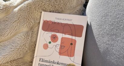 Kuvassa teos Elämänkokemuksen tunnejäljet on tuolin päällä aurinkoisella terassilla. Tuolilla on myös pörröinen viltti. Taustalla näkyy valkoinen rimakaide ja kaiteen takana vihreää pihaa.