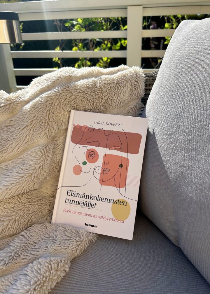 Kuvassa teos Elämänkokemuksen tunnejäljet on tuolin päällä aurinkoisella terassilla. Tuolilla on myös pörröinen viltti. Taustalla näkyy valkoinen rimakaide ja kaiteen takana vihreää pihaa.