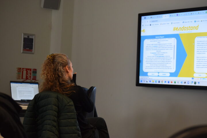 A woman looks at a screen. On the screen is the Endostand app, produced by the #ENDOs project.