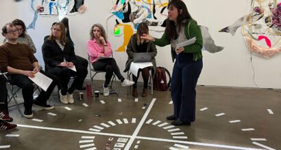One woman stands in the centre of a large compass. A group listen to her instructions.