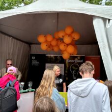 ENERGIAA!-hankkeen telttakoju, jossa edessä ihmisiä selkä kuvaajaan päin ja katossa oransseja ilmapalloja.