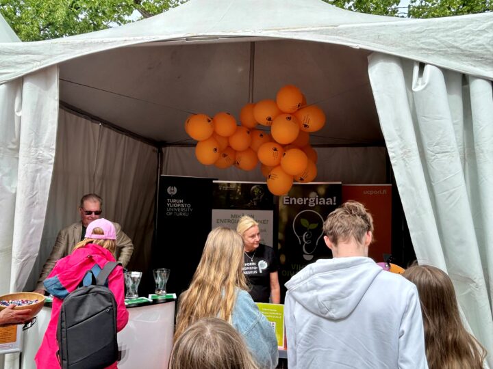 ENERGIAA!-hankkeen telttakoju, jossa edessä ihmisiä selkä kuvaajaan päin ja katossa oransseja ilmapalloja.