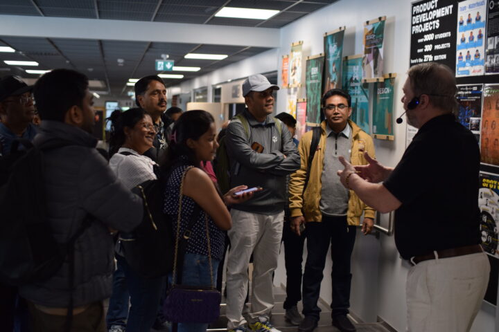 A group of people are listening to the presentation of a middle-aged man wearing a wireless headset. 