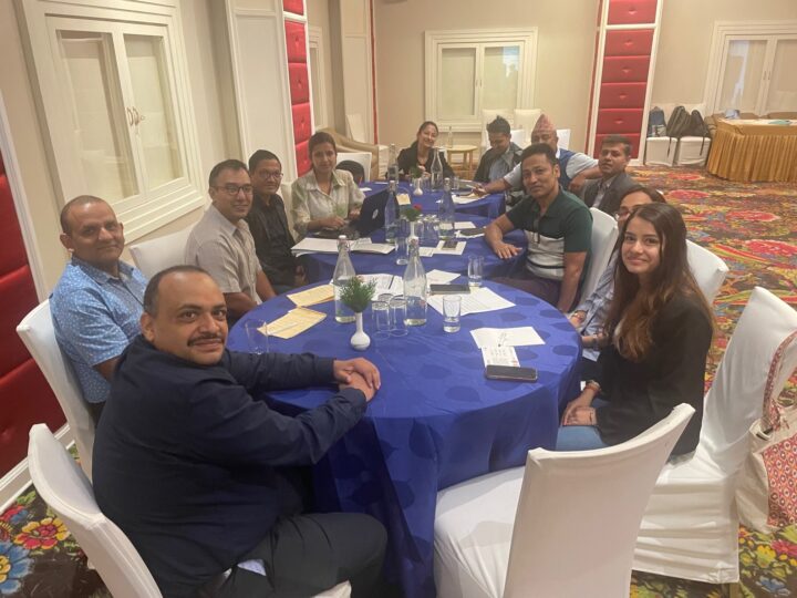 A group of twelve adults gathered around table filled that has papers, water and glasses on them. The people look at the camera smiling. 