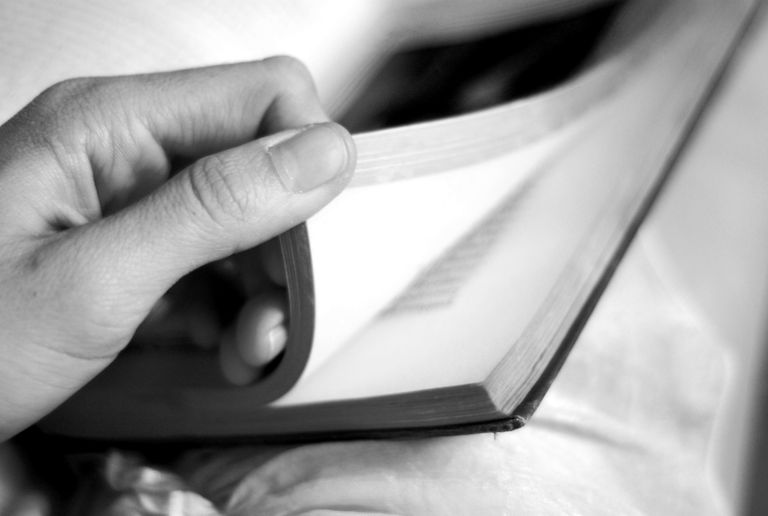 Artistic black and white close-up of a hand gently turning a book page, conveying contemplation and learning.