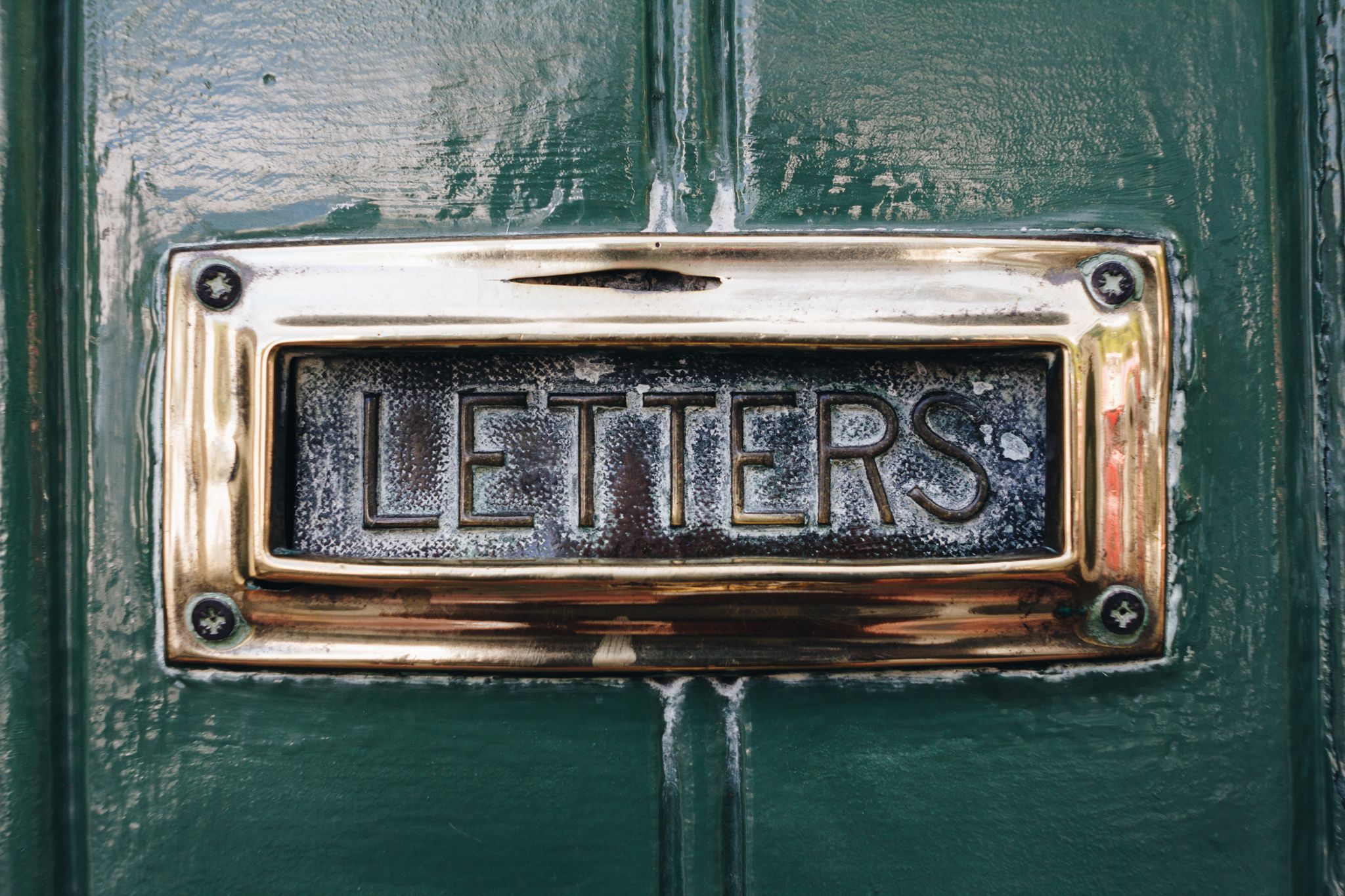Close-up of an antique mail slot labeled 'letters' on a painted green door.