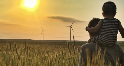 Aikuinen ja lapsi katselevat tuulivoimaloita pellolla