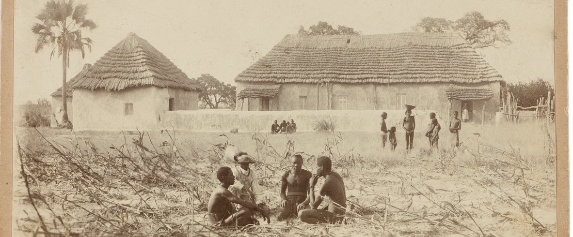 vanha valokuva, jossa etualalla afrikkalaisia ihmisiä ja taustalla eurooppalaistyylisiä rakennuksia