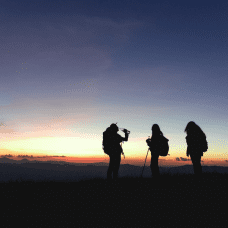 Picture of three people standing on top of a hill and watching sunset