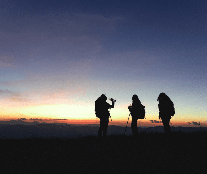 Picture of three people standing on top of a hill and watching sunset