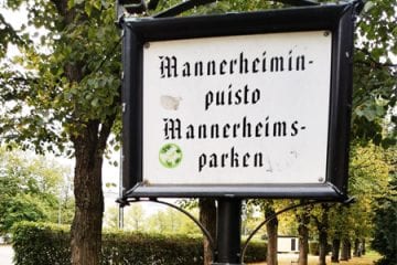 Kaksikielinen puiston nimikyltti kesäisessä Mannerheimin puistossa.