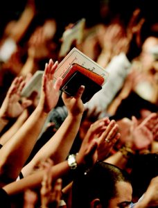 Suuri määrä ihmisiä nostaneena kädet ylös ylistykseen, yhdellä kädessään Raamattu.