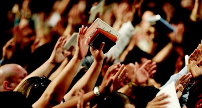 Suuri määrä ihmisiä nostaneena kädet ylös ylistykseen, yhdellä kädessään Raamattu.