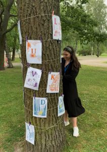 Nainen katselemassa puunrunkoon kiinnitettyjä Tove Janssonin tekemiä kuvituksia Kupittaanpuistossa