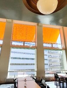 Kuvassa lämpimässä auringonvalossa kylpevä ruokasali pöytineen. Ikkunoista näkyy vastapäinen potilassiipi. Kuva: Emma Uola