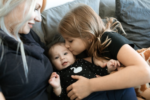 Äiti, vauva ja lapsi yhdessä sohvalla