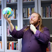 A man in a purple shirt holds a globe toy in a dramatic way.