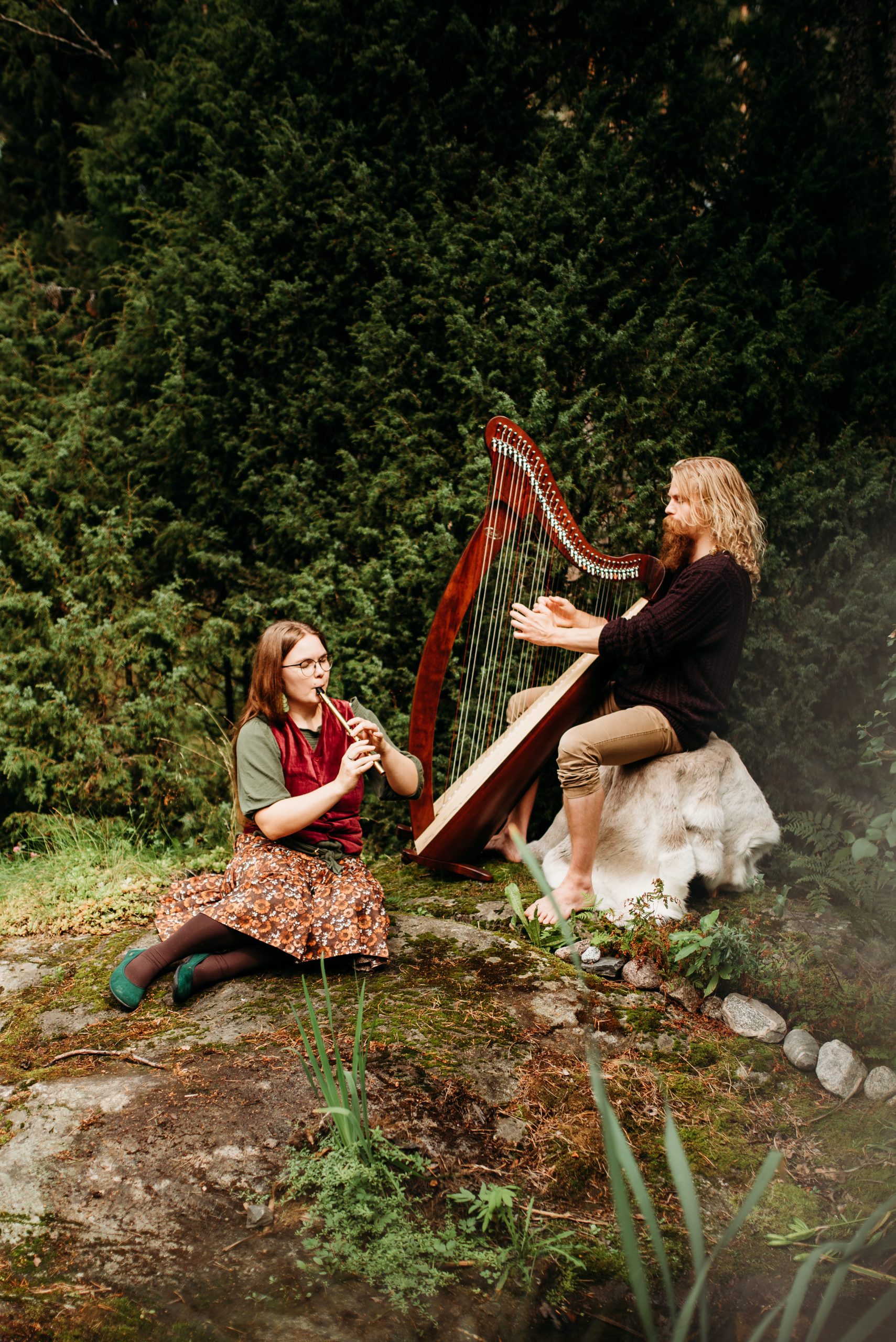 Kaksi henkilöä soittamassa huilua ja harppua metsässä.