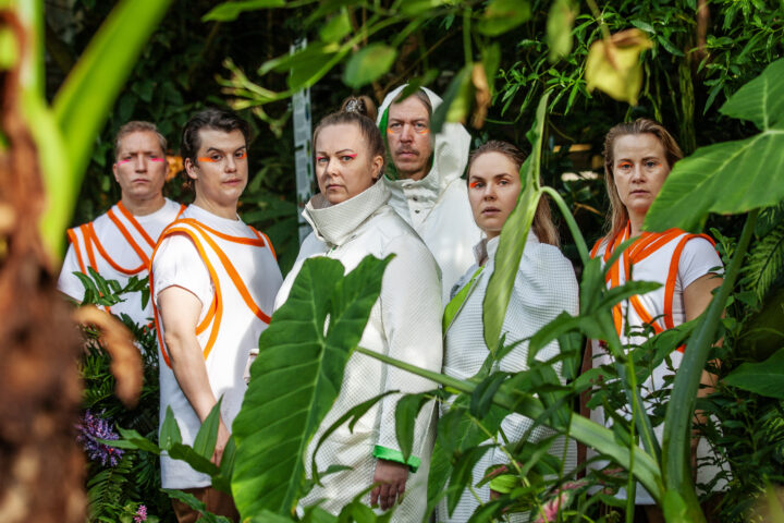 Ryhmäkuva esiintyjistä kasvihuoneessa.