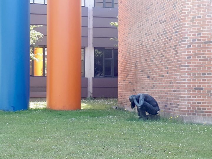 The picture shows a statue crouching by a building wall, holding its head.