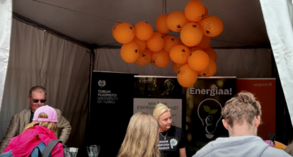 ENERGIAA!-hankkeen telttakoju, jossa edessä ihmisiä selkä kuvaajaan päin ja katossa oransseja ilmapalloja.