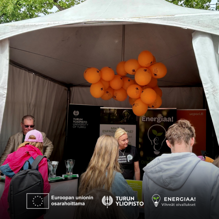 ENERGIAA!-hankkeen telttakoju, jossa edessä ihmisiä selkä kuvaajaan päin ja katossa oransseja ilmapalloja.