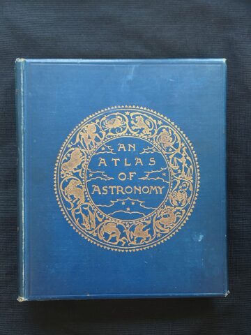 Kuvassa on kirjan etukansi. Kansi on sininen ja sen keskellä on kultaisessa kehässä 12 horoskooppimerkkiä. Kehän keskellä on kirjan nimeke ”An Atlas of Astronomy”, sekin kullan värinen.