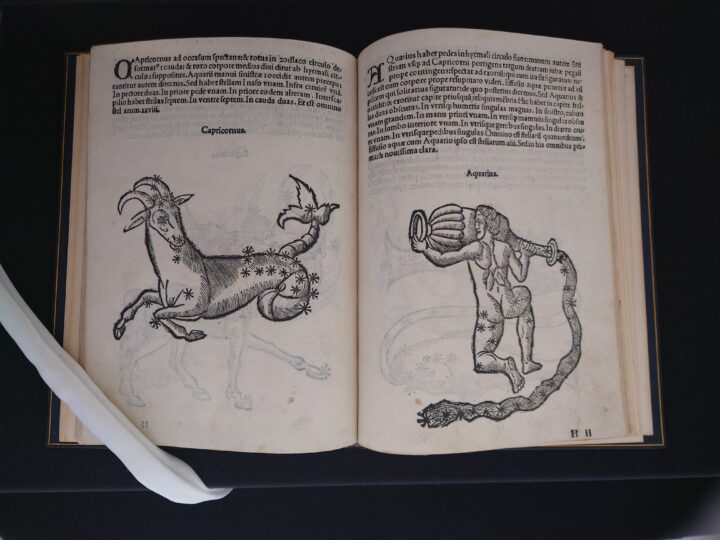 The picture shows the opening of a book. On both pages the text is printed at the top of the page and at the bottom are pictures of constellations. On the left-hand page, the constellation of capricornus is shown. The picture shows an animal with a goat's front body and a snake-like tail. On the right is an aquarius. The naked male figure is kneeling, carrying a large pot from which water is flowing down past him.