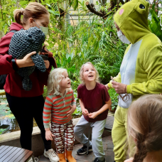 Lapset innoissaan sammakkopukuisen ohjaajan vieressä Turun yliopiston kasvitieteellisellä puutarhalla.