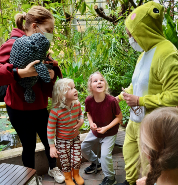 Lapset innoissaan sammakkopukuisen ohjaajan vieressä Turun yliopiston kasvitieteellisellä puutarhalla. 