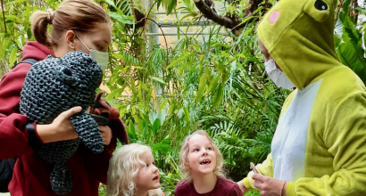Lapset innoissaan sammakkopukuisen ohjaajan vieressä Turun yliopiston kasvitieteellisellä puutarhalla.