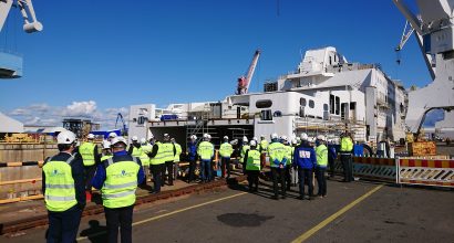 Lots of people with yellow vests in front of a ship in a shipyard.