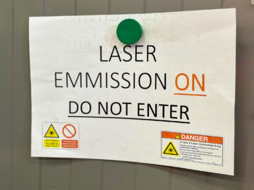 A4-kokoinen paperi-ilmoitus seinässä varoittamassa lasertyöstön olevan käynnissä eikä saa mennä sisään.
