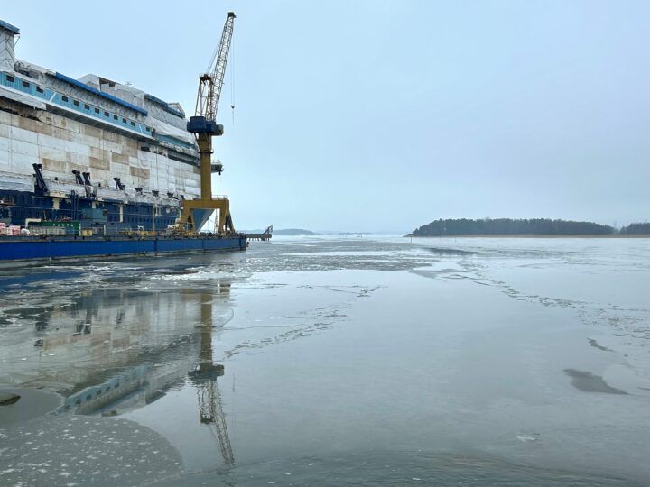 Rakenteilla oleva laiva, nosturi ja sen heijstu jäähän sekä saarimaisema.