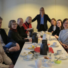 Hymyileviä ihmisiä kahvipöydän ympärillä katse kohti kuvaajaa.