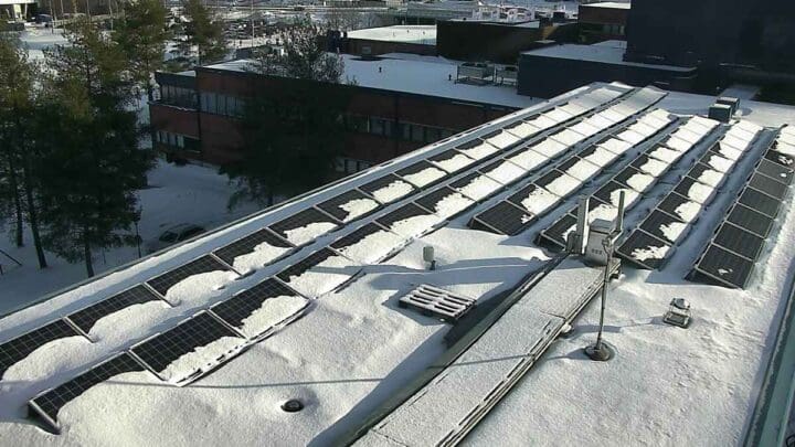 Osittain lumen peittämiä aurinkopaneeleja lumisen katon päällä Kuopiossa.