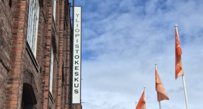 Punainen tiilirakennus, teksti Yliopistokeskus, pilviä taivaalla