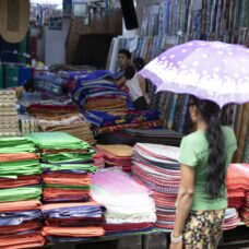 A woman stands in front of a market stall with an umbrella