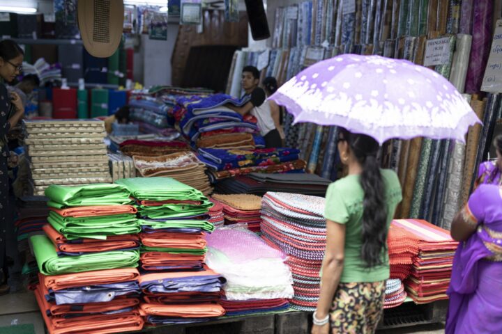 A woman stands in front of a market stall with an umbrella