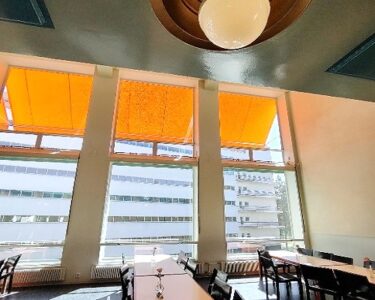 Kuvassa lämpimässä auringonvalossa kylpevä ruokasali pöytineen. Ikkunoista näkyy vastapäinen potilassiipi. Kuva: Emma Uola