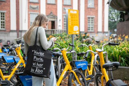Opiskelija seisoo Turun kaupunginkirjaston pyöräparkin edessä olallaan kangaskassi, jossa on teksti ”Varför Paris, vi har ju Åbo”.