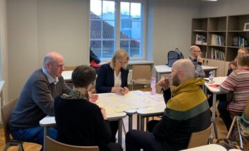 Työryhmän jäsenet istuvat pöytien ääressä keskustelemassa ja tekemässä ryhmätöitä.