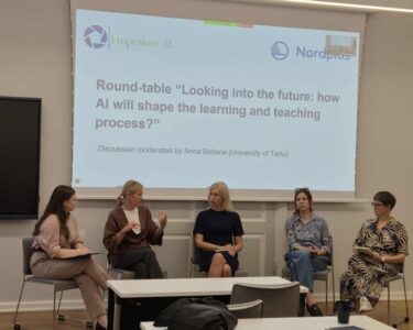 Kuvatekstissä mainitut panelistit istuvat rivissä luentosalin etuosassa ja taustalla näkyy dia, jossa on teksti: Round-table ”Looking into the future: how will AI shape the learning and teaching process?”