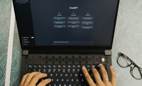 Kuvassa näkyy sormet kannettavan tietokoneen näppäimistöllä ja auki on ChatGPT.