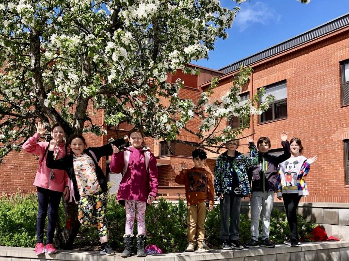 Oppilata heiluttamassa koulupihalla omenapuun juuressa